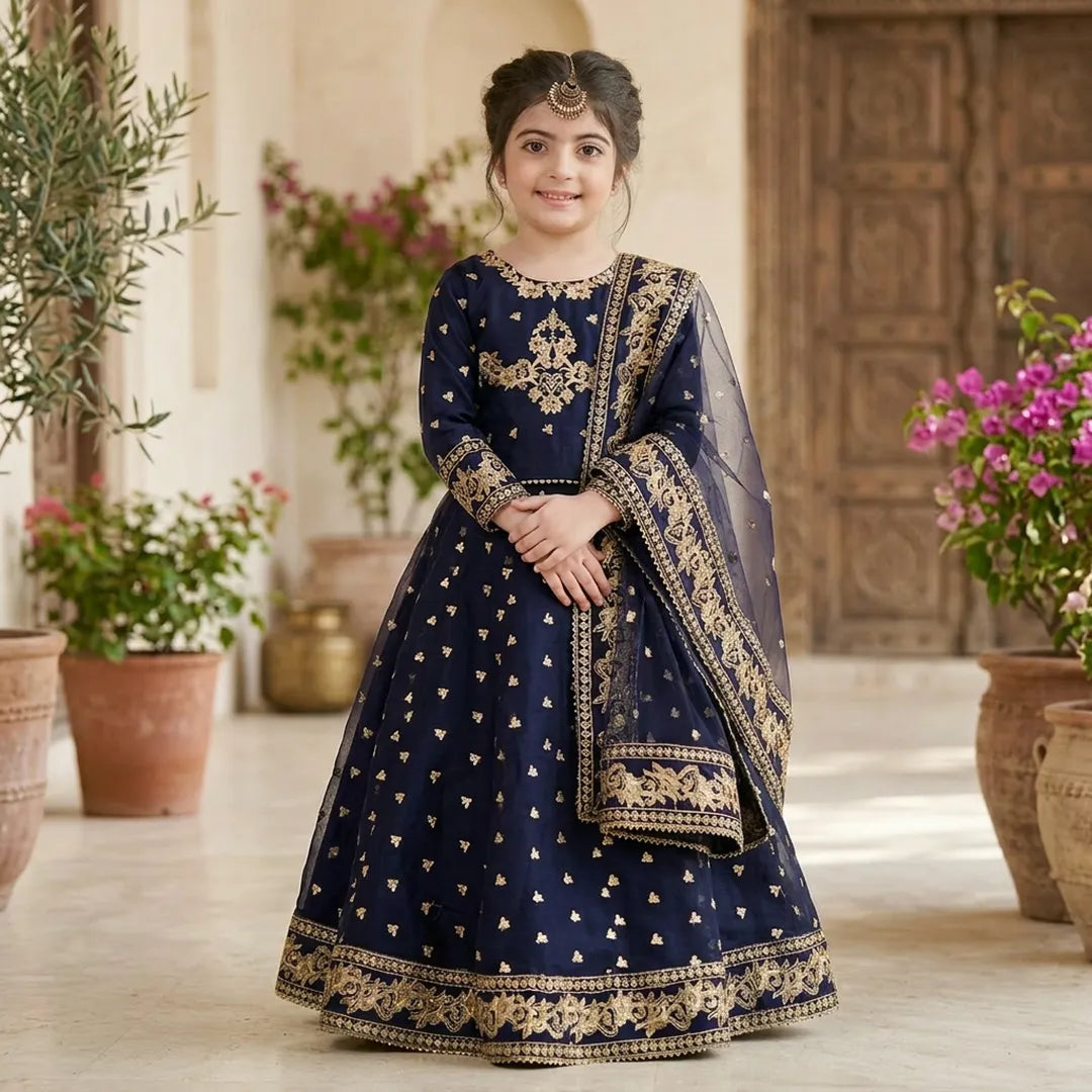Woman in a traditional navy blue and gold embroidered outfit standing in a decorative indoor setting with plants.