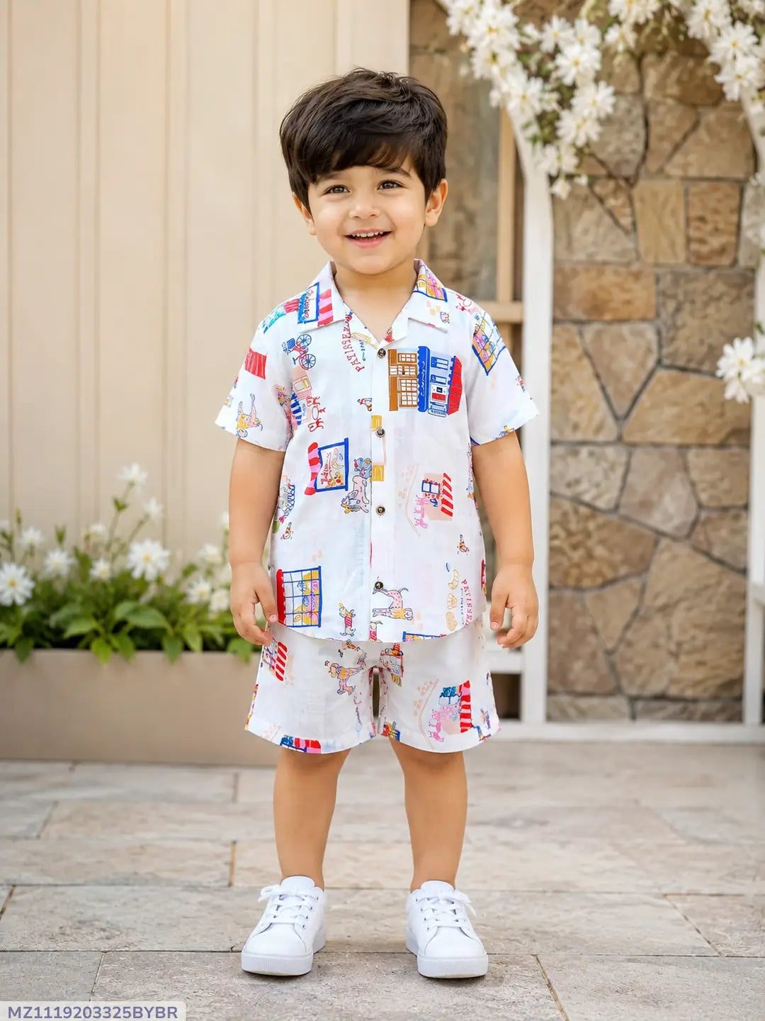 Child wearing a colorful outfit standing outdoors with flowers and a stone wall in the background