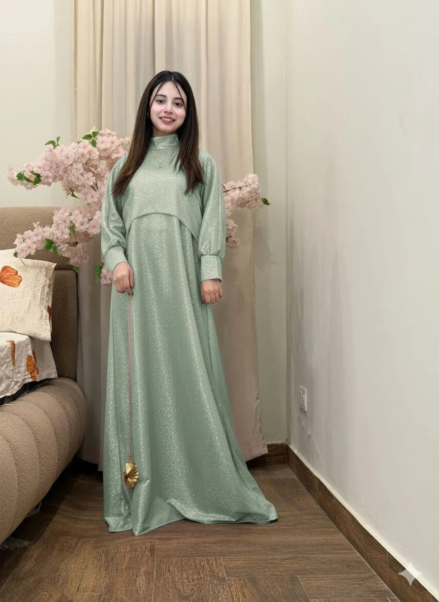 Woman in a long green dress standing in a room with floral decorations.
