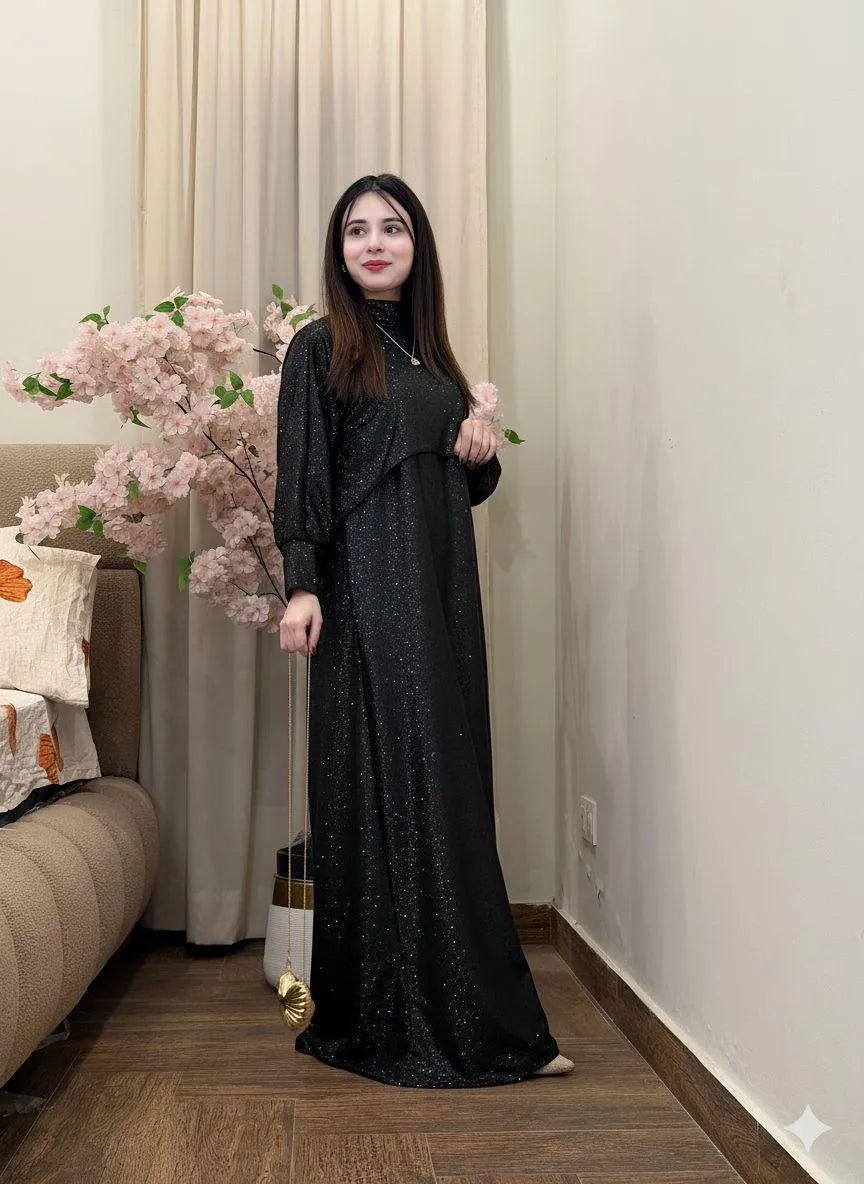 Woman in a black dress standing in a room with a couch and decorative flowers.